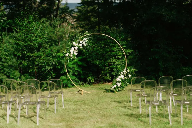   Julie et Miguel's outdoor ceremony with a gold arbor covered in flowers and ghost chairs