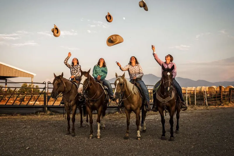   Neljä naista hevosten selässä heittää cowgirl-hattuja ilmaan.