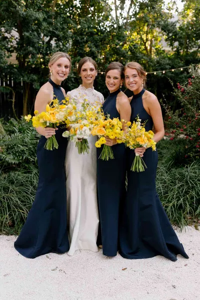   Greer's bridesmaids in halter navy dresses carrying yellow bouquets