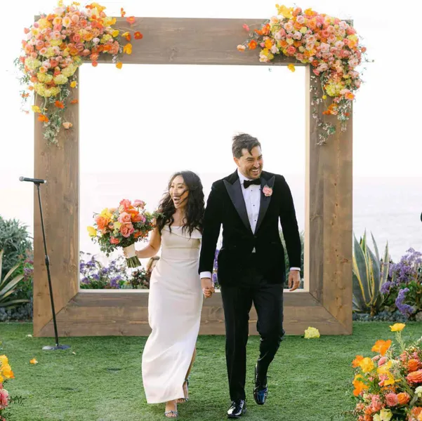   récréation des mariés après le mariage avec une arche en bois et des fleurs aux couleurs du coucher du soleil