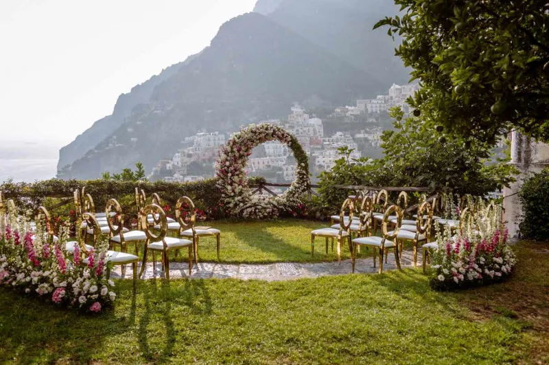   Rosa ja Keith's ceremony overlooking the town of Amalfi with a floral circular arch and gold chairs