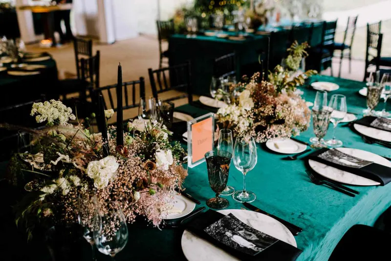   Alex e Uche's teal tablecloths, marble chargers, orange table numbers, black flatware, black napkins, and dried centerpieces
