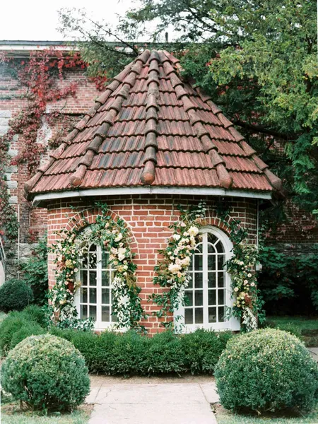   గ్రేస్ మరియు JP's ceremony setup in an English garden with the building exterior decorated with flowers