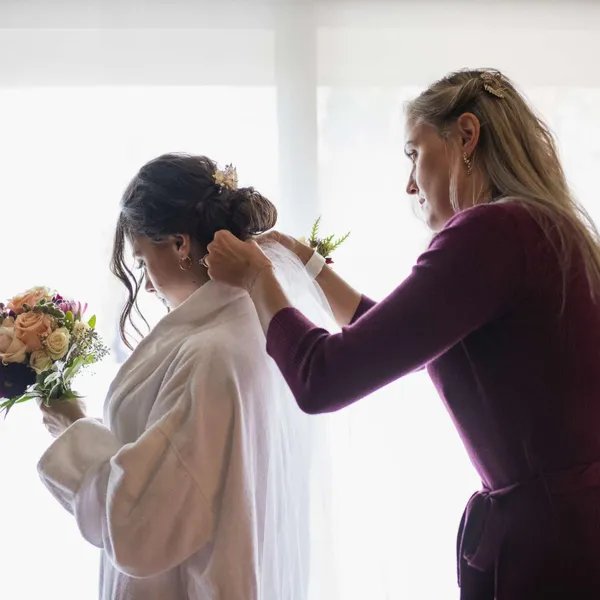   Un accompagnateur personnel lors d'un mariage aide la mariée à ajuster son voile tout en se préparant.