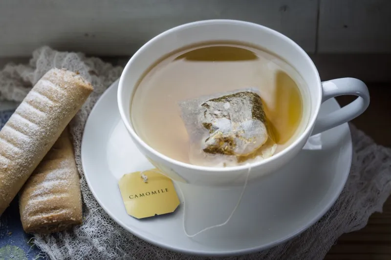   Une tasse à thé blanche et une soucoupe avec un sachet de thé et des biscuits.