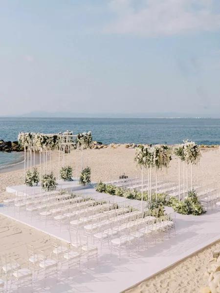   Brittani ja Jared's beach ceremony with a glamorous floral setup and white chairs