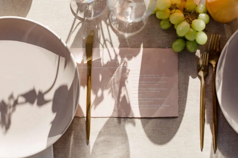   Mégane et Thomas's place settings with gold flatware, pink menus, and modern chargers