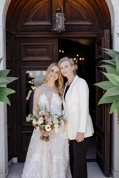   Megan dans sa robe de mariée en dentelle souriant avec sa tante dans un blazer blanc