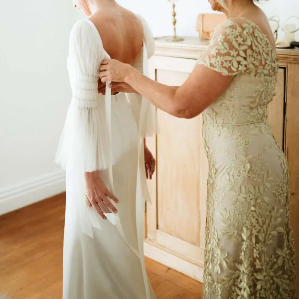   mariée aidant sa fille à enfiler sa robe de mariée