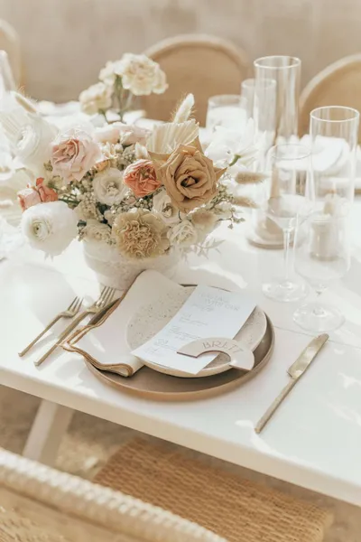   Kenzie i Jake's place settings with beige chargers, semicircular place cards, folded napkins, and gold flatware