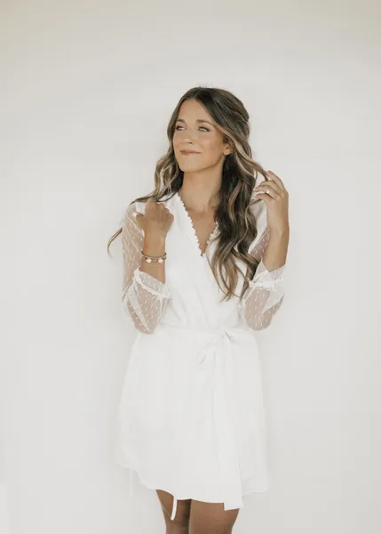   Kenzie's white robe with sheer sleeves, natural makeup, and wavy hair in a half-up hairstyle