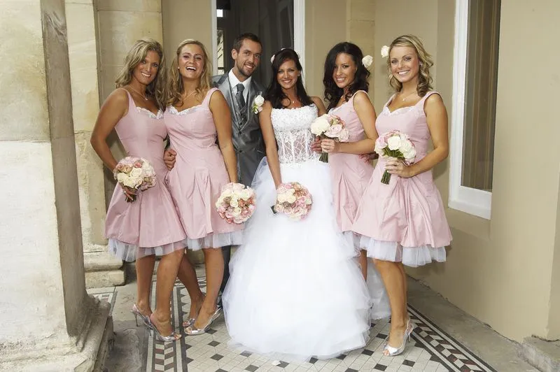   Les demoiselles d'honneur en robes roses se tiennent avec la mariée en robe de mariée et le marié en smoking gris dans l'émission TLC Four Weddings.