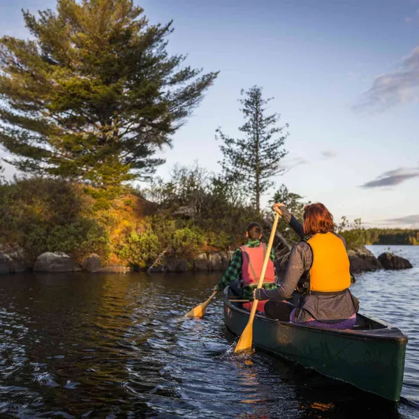   Un couple portant des gilets de sauvetage pagaie dans un canot vert vers une petite île sur un lac du Maine.