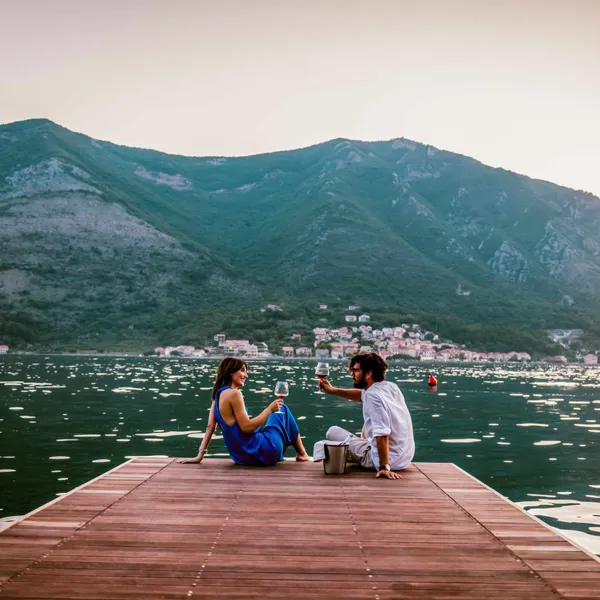   Un couple sirote du vin assis sur un quai en bois surplombant un lac et des montagnes en Italie.