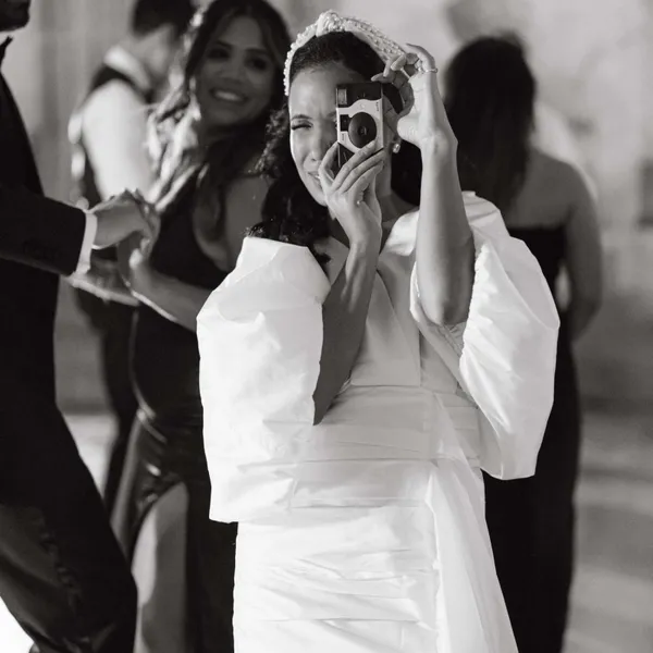   Photo en noir et blanc d'une mariée prenant une photo avec un appareil photo jetable lors de son mariage.