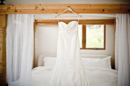   Robe de mariée blanche accrochée dans une chambre blanche sur un cadre de lit en bois